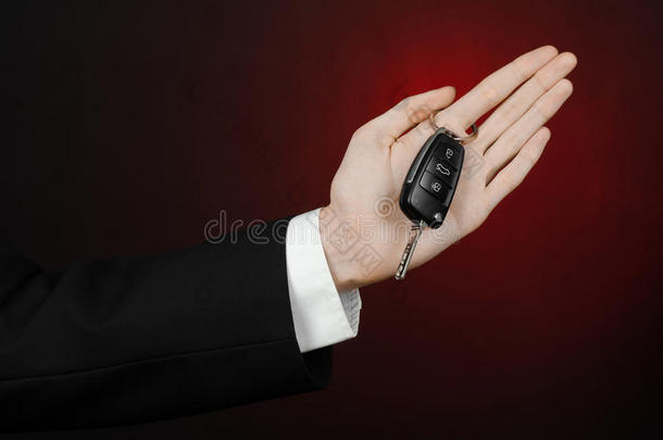 商业和礼物主题：穿着黑色西装的汽车推销员在工作室的深红色背景上拿着一辆新车的钥匙