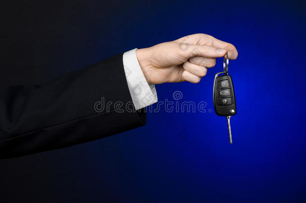 商业和礼物<strong>主题</strong>：穿着黑色西装的<strong>汽车</strong>推销员在工作室的深蓝色背景上拿着一辆新车的钥匙