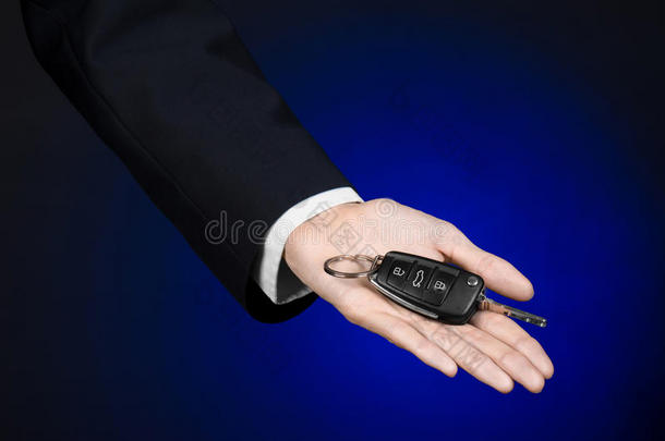 商业和礼物主题：穿着黑色西装的汽车推销员在工作室的深蓝色背景上拿着一辆新车的钥匙