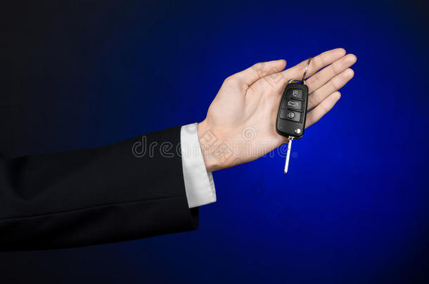 <strong>商业</strong>和礼物主题：穿着黑色西装的汽车推销员在工作室的深<strong>蓝色背景</strong>上拿着一辆新车的钥匙