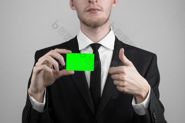 商人穿着黑色西装和黑色领带拿着一张卡片，一只手拿着一张卡片，绿卡，卡片被插入，绿色的色度