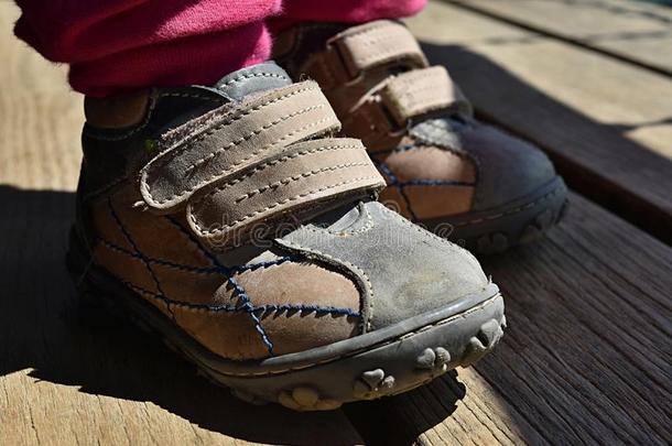 穿着米色尼龙搭扣靴子的小女孩的脚站在木地板上