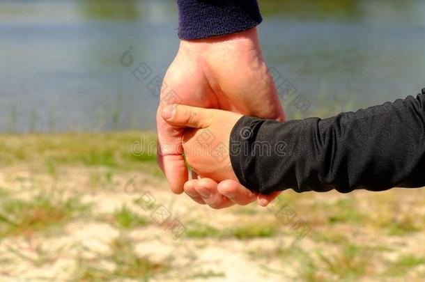 父亲的大手牵着一个孩子的手。 手穿蓝色和黑色衬衫。