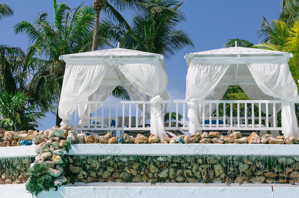 在阳光明媚的一天，热带花园里有两个白色舒适的凉亭的特写镜头