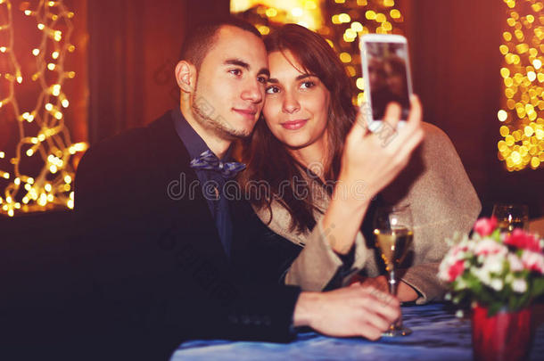 一对相爱的漂亮夫妇坐在餐馆里，用智能手机拍一张自拍照片