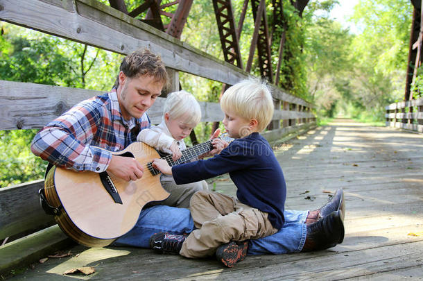 父亲和两个孩子在公园外面弹吉他