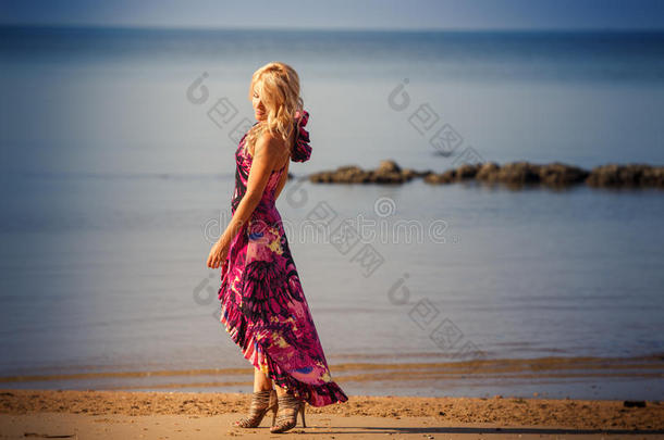穿紫色连衣裙的金发女孩在海滩上散步