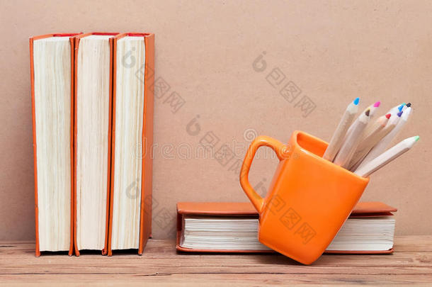一叠书和一个木桌上有彩色铅笔的杯子