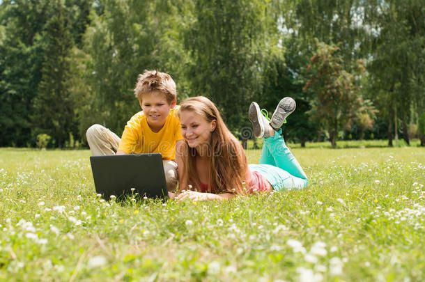 男孩和女孩坐在草地上，带着笔记本<strong>电脑</strong>，在公园上网。 <strong>两个</strong>微笑的青少年学生带着笔记本<strong>电脑</strong>在草地上休息。 教育