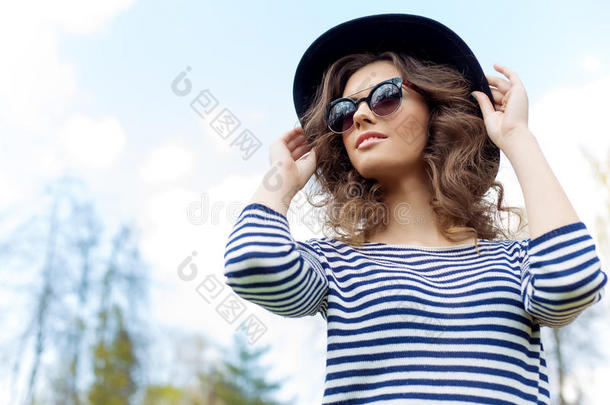 明亮美丽的年轻快乐的女孩戴着帽子和太阳镜在阳光明媚的一天在公园里散步