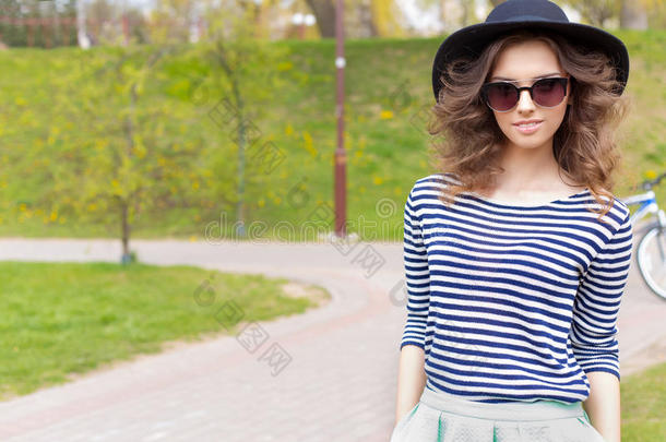 明亮美丽的年轻快乐的女孩戴着帽子和太阳镜在阳光明媚的一天在公园里散步