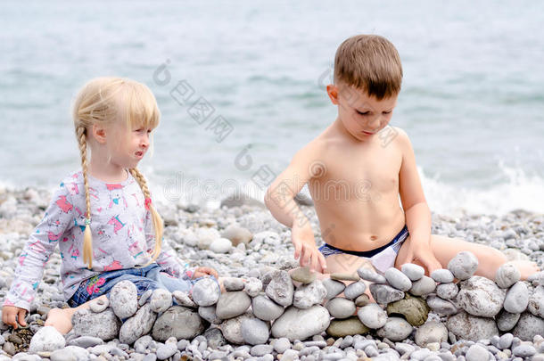 男孩和女孩在岩石海滩上建造石墙