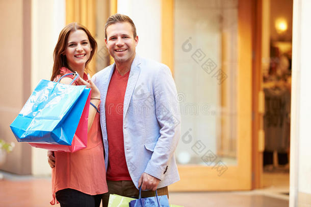 一对夫妇站在商场外面的商店里拿着购物袋