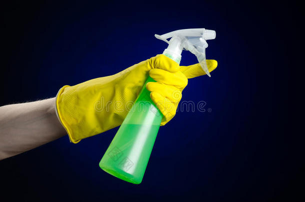 清洁房子和清洁主题：男人的手戴着一只黄色手套，拿着一个绿色的喷雾瓶，用深蓝色清洗