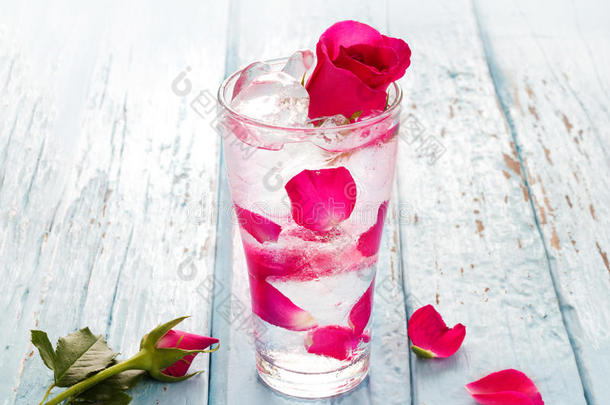 蓝色木制背景上玫瑰花瓣的玻璃美味清爽饮料