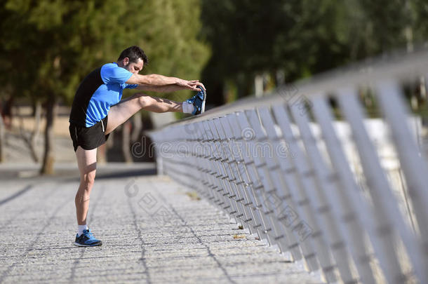 运动员男子伸展腿，热身小腿肌肉，然后跑步锻炼，靠在栏杆城市公园
