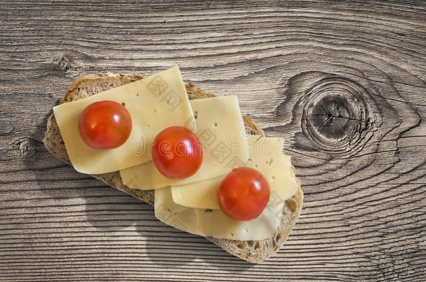 奶酪三明治与三个樱桃西红柿装饰在旧的结粗糙的松木桌子上