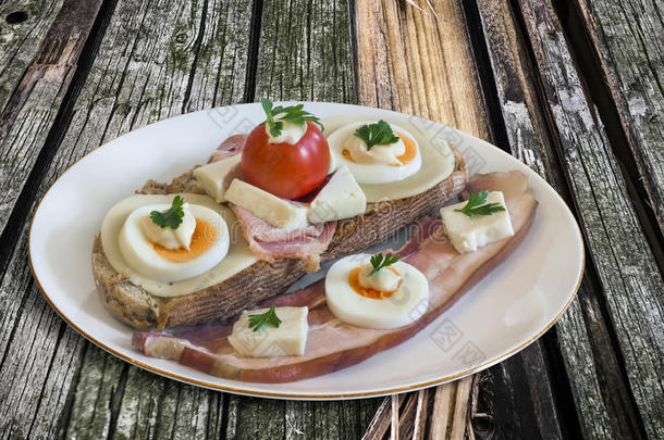 培根和鸡蛋三明治与额外的腹部培根碎肉提供在瓷盘上设置在旧的开裂松木野餐桌