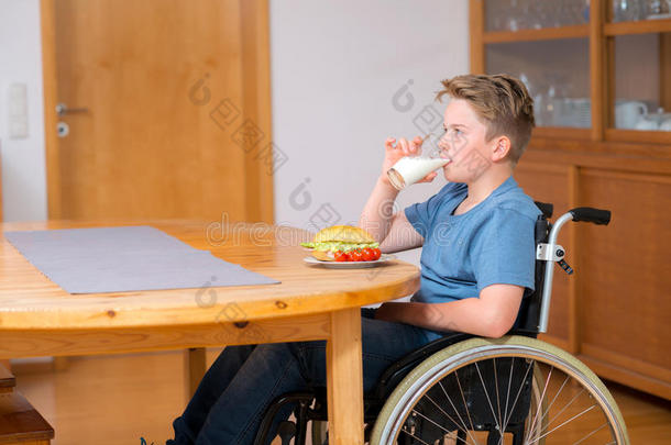 坐轮椅的残疾男孩正在喝牛奶和吃饭