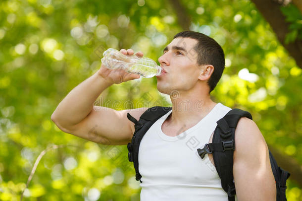 活跃的人从瓶子里喝水，户外。 年轻的肌肉男会止渴