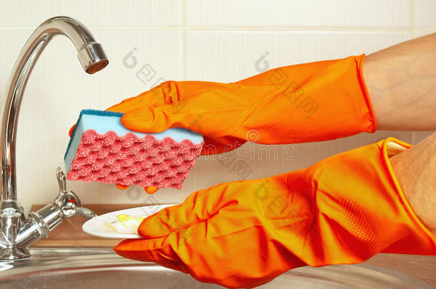 双手戴手套，用海绵和<strong>脏盘子</strong>在厨房的水槽上