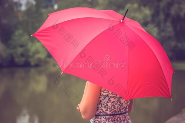 在池塘附近带着红色雨伞的女孩