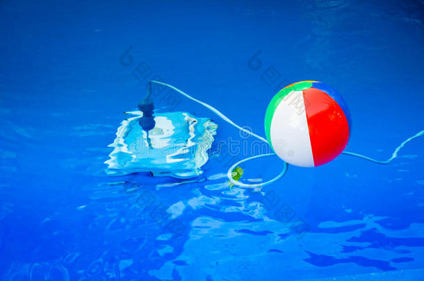 五颜六色的沙滩球漂浮在游泳池里，旁边有一个清洁机器人