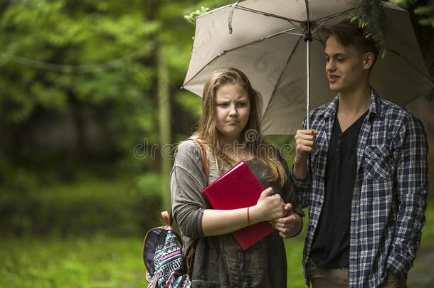 一对夫妇在户外聊天。 手里拿着一本红色的书的女孩和拿着雨伞的家伙。