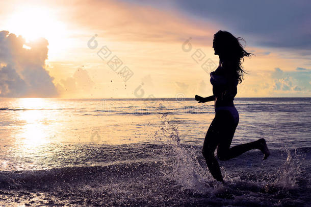 无忧无虑的女人在海滩上的夕阳中奔跑