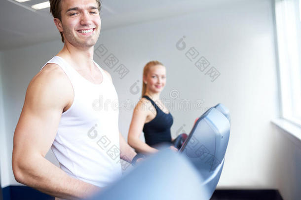 在跑步机上运动的年轻人对着摄像机微笑