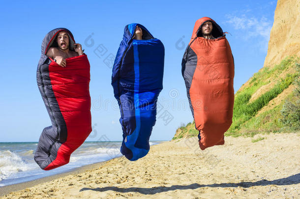 一群欢呼的徒步旅行者在海边跳着<strong>睡袋</strong>