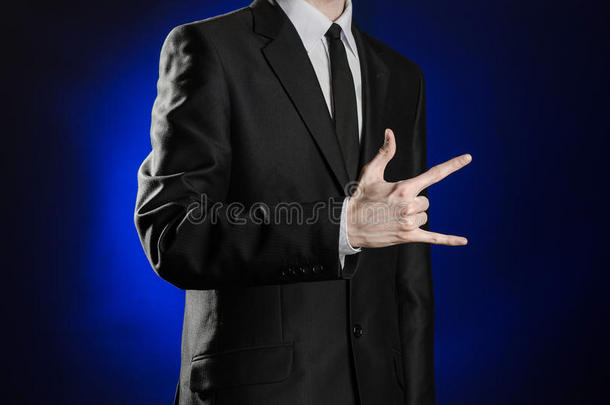 商业和主题的展示：穿着黑色西装的人在工作室孤立的深蓝色背景上展示手势