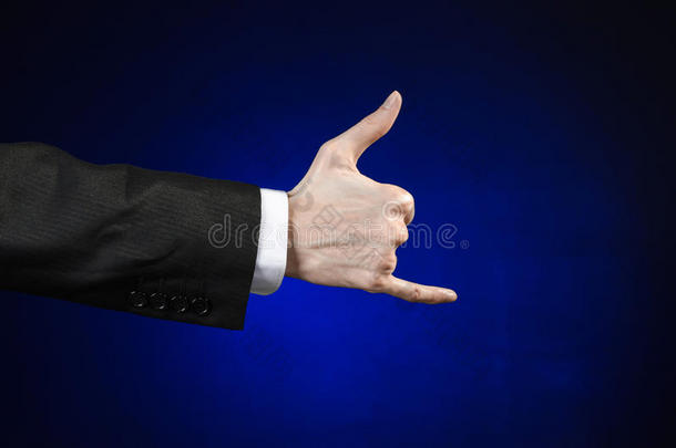 商人和手势主题：一个穿着黑色西装和白色衬衫的男人在一个孤立的深蓝色背景上展示手势