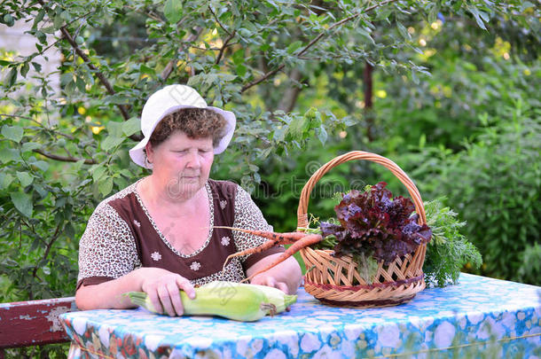 一位老妇人拿着一篮子蔬菜坐在桌子旁