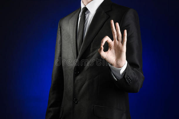 商人和手势主题：一个穿着黑色西装和白色衬衫的男人在工作室的深蓝色背景上展示了好的手势