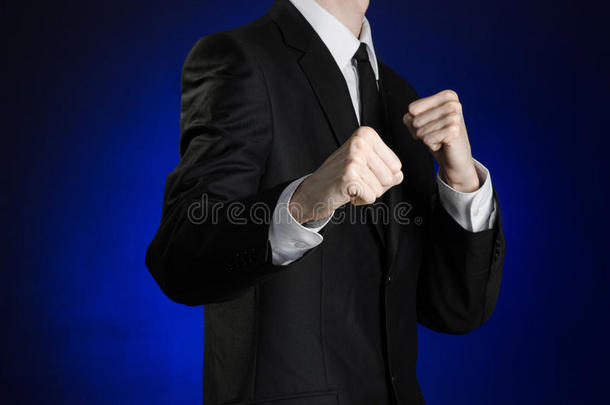 商人和手势主题：一个穿着黑色西装和白色衬衫的人在深蓝色的背景下，握着拳头在他面前