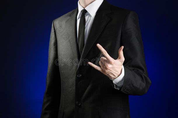 《生意人与手势》主题：演播室里，一个身穿黑色西装和白色衬衫的男人在深蓝色背景上展示一块手牌石头