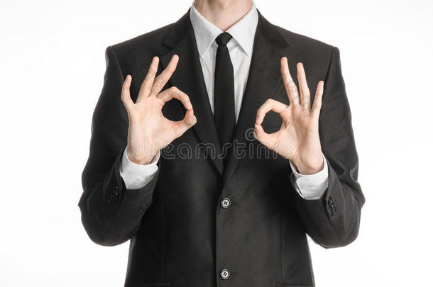 商人和手势主题：一个穿着黑色西装，打着领带的人，在斯图的白色背景上显示出两只手的OK标志