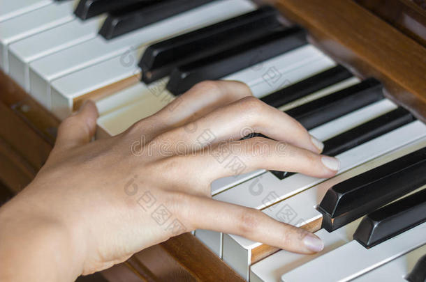 女孩的右手手指握着钢琴上的按键