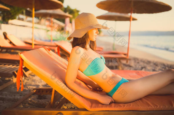 美丽的女人在热带旅游胜地的海滩上穿着比基尼晒太阳，享受暑假。年轻的女人躺在太阳床上