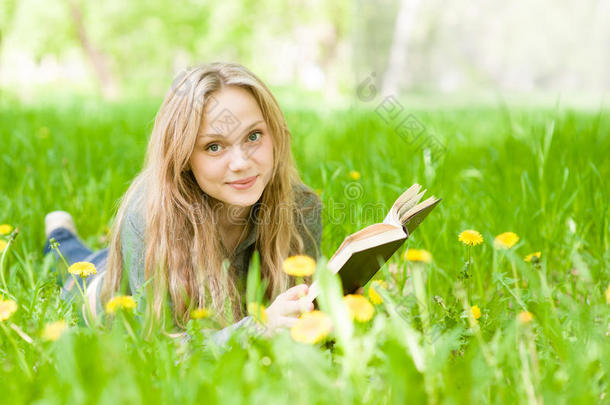 女孩躺在草地上，蒲公英在读一本书，看着相机