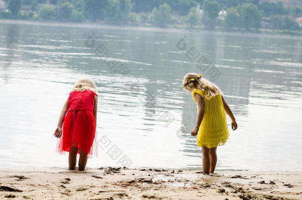 穿着红色连衣裙和黄色连衣裙的金发女孩在河边