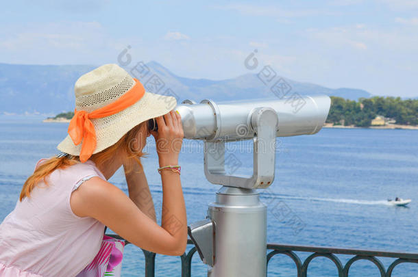 在<strong>海边</strong>透过公共望远镜看的女孩穿着粉<strong>红色</strong>的衣服