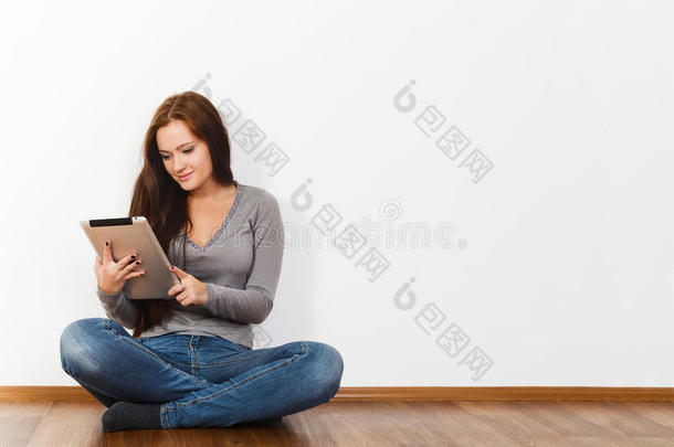 漂亮的年轻女人坐在地板上拿着平板电脑