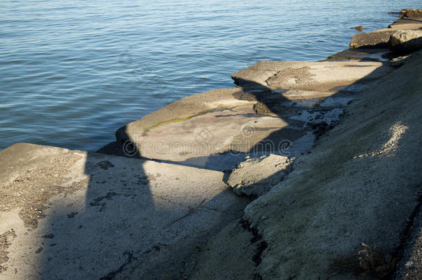 下午晚些时候，在平静的海洋湾边缘有棱角的破碎混凝土板。
