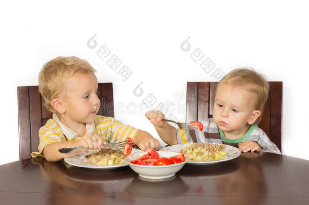 金发小男孩试图用叉子土豆和肉和西红柿吃饭