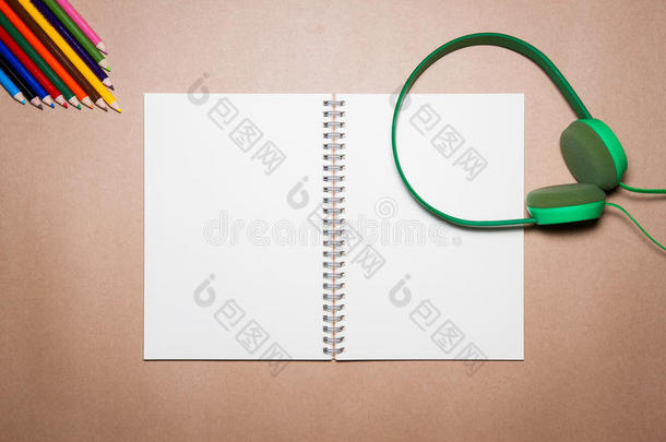 棕色纸上的绿色耳机、笔记本、钢笔和彩色铅笔。