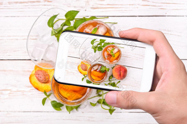 双手拍照冰茶与桃子与智能手机。