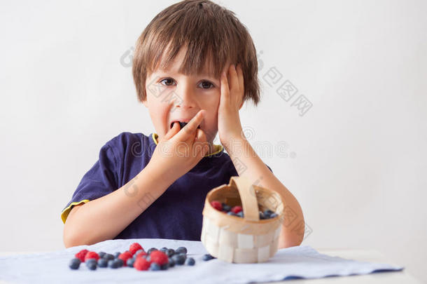 孩子，坐在桌子后面，桌子上有树莓和蓝莓