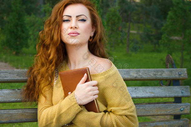 <strong>姜黄色</strong>头发的女人拿着书坐在长凳上